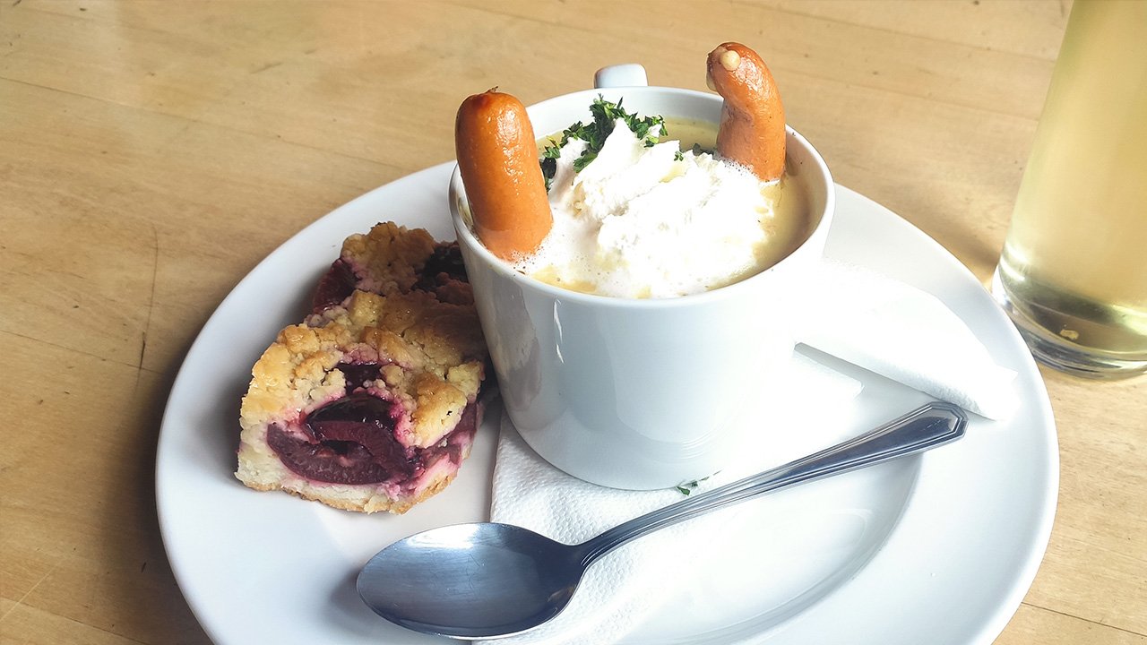 Herzhafte Suppe mit Würstchen und süßer Pflaumenkuchen auf Holztisch, dazu ein Glas Weißwein.