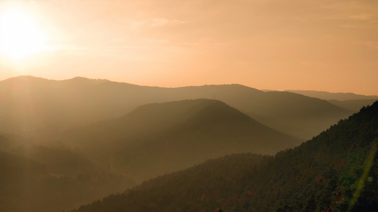 Herbstliche Abendstimmung in den Bergen: goldener Sonnenuntergang über nebelverhangenen Hügeln und Tälern.